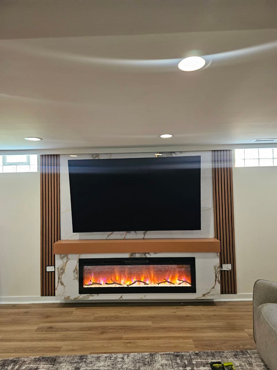 Media wall with marble-look panel, wood slat trim, TV mount, and built-in fireplace