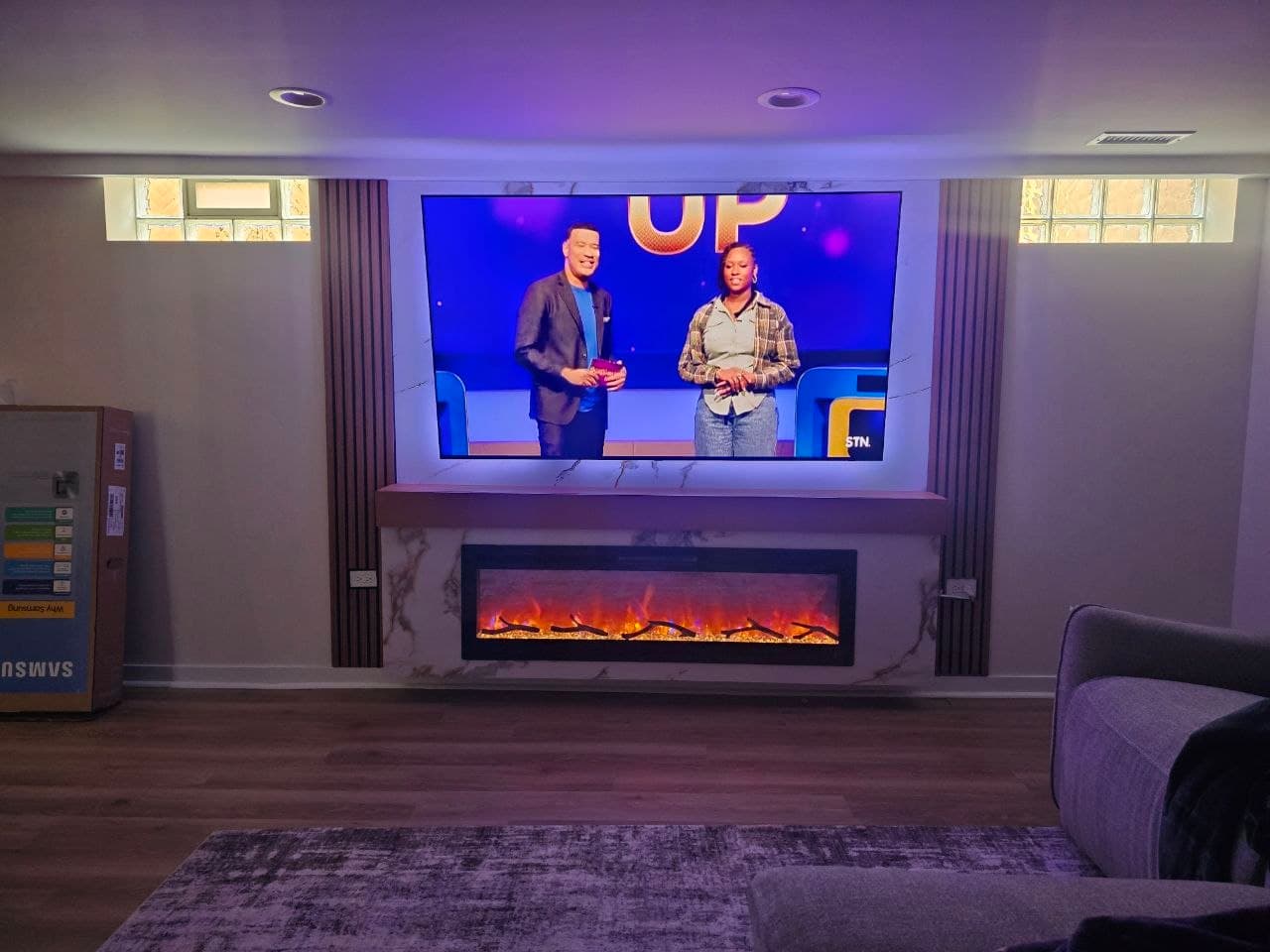 Marble and wood slat media wall with TV on, above a linear electric fireplace