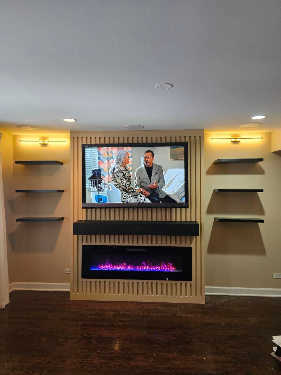 Tan wood slat media wall with floating shelves either side of a mounted TV and fireplace