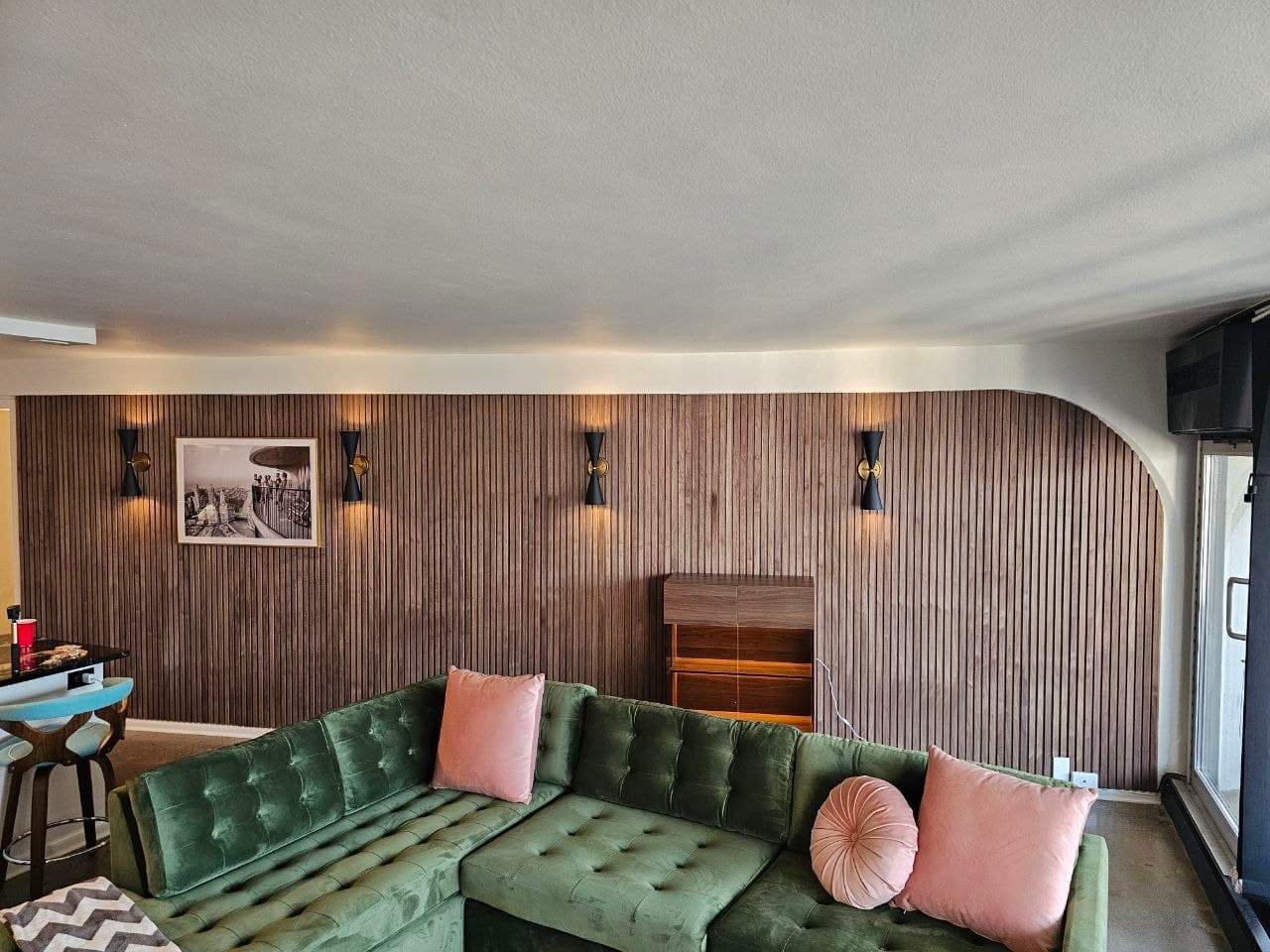 Wide view of a walnut wood slat accent wall with sconces and framed print